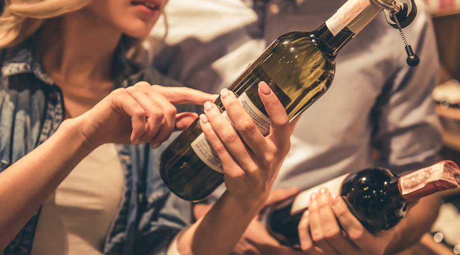 Two individuals examining and discussing bottles of wine.